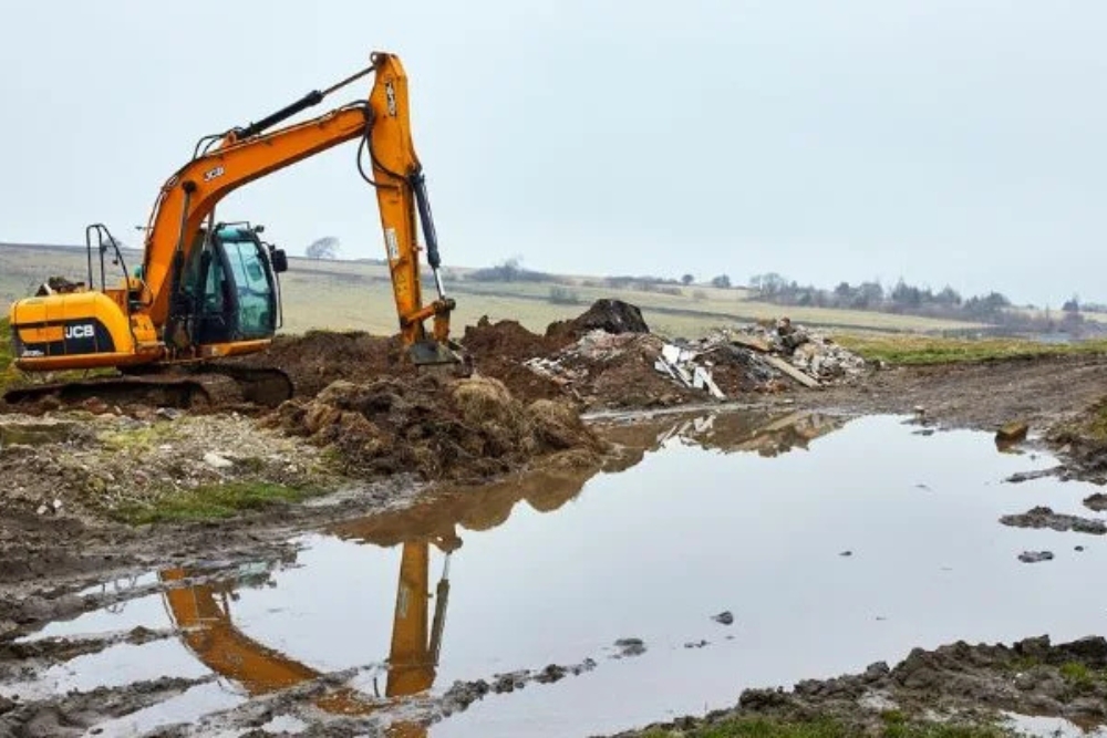 Tracked excavator clearing spoil and debris on a wet open site during site preparation